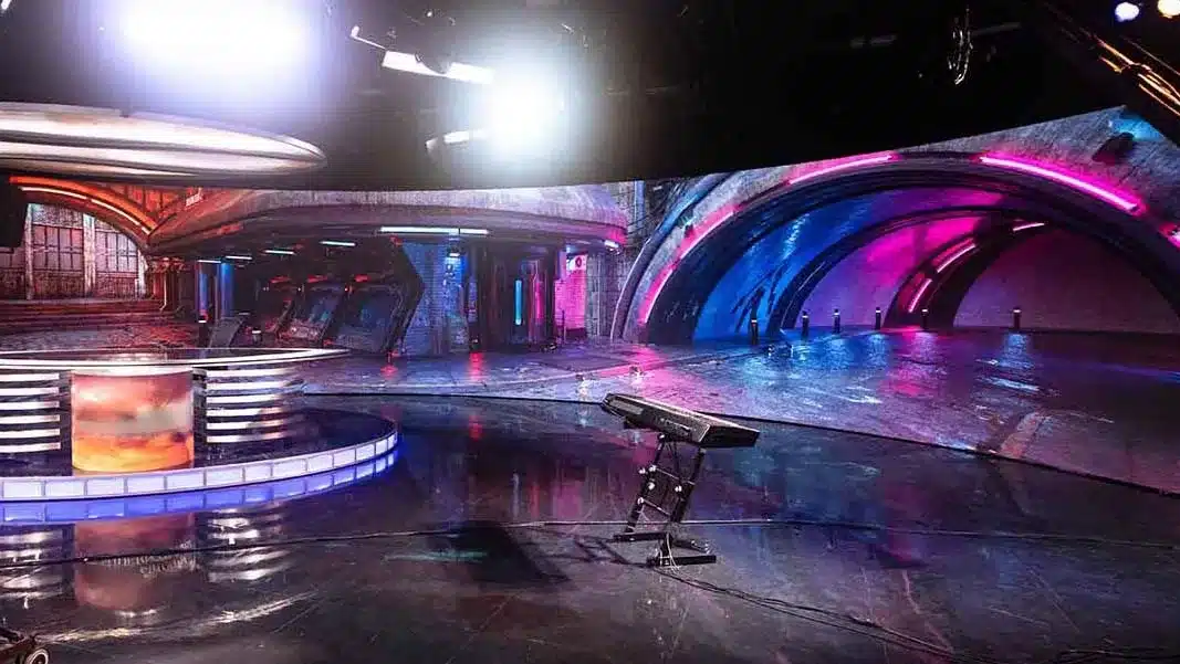 Futuristic TV studio with neon-lit arches, reflective floor, LED desk, & keyboard stand